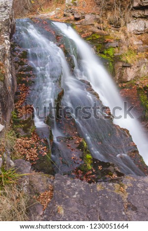 Gorgeous mountain creek waterfall cascading down the rocky cliff and colorful autumn red leaves, close-up