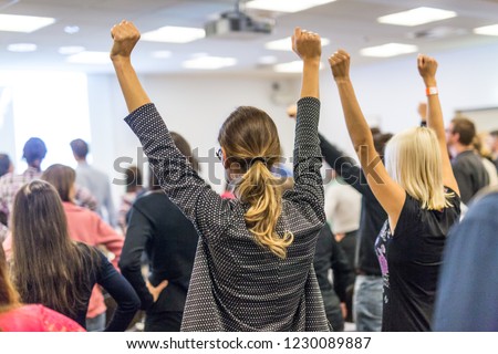 Life coaching symposium. Speaker giving interactive motivational speech at business workshop. Rear view of unrecognizable participants feeling empowered and motivated, hands raised high in air. Royalty-Free Stock Photo #1230089887
