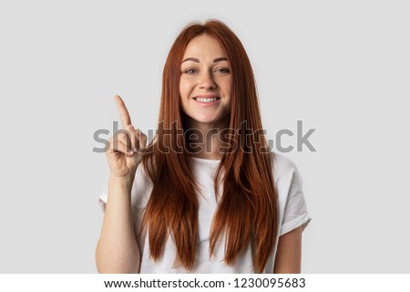 I have an idea! Beautiful redhead woman keeping finger pointed upwards, showing something above her head, making gesture with index finger. Eureka, solution sign concept