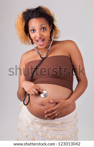 Pregnant african woman listening her baby with a stethoscope , over white background