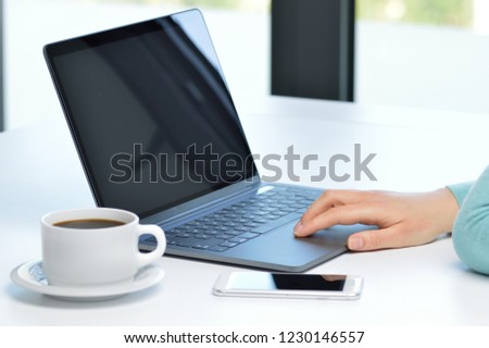 Back light close up of a lady hand browsing websites in a laptop sitting in a desktop in a house with a window in the background