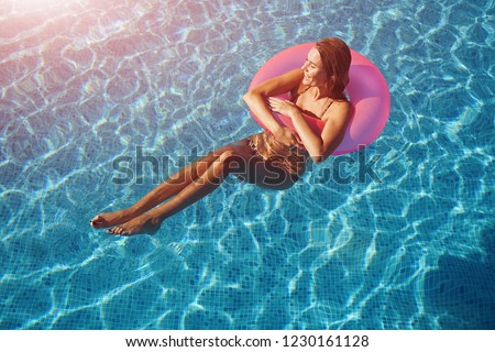 Young beautiful model relaxing with a pink swim ring in a blue water of swimming pool.