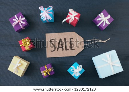 shopping banner with text word Sale on cardboard label with multicolored gift boxes on dark background. Black Friday sale shopping concept