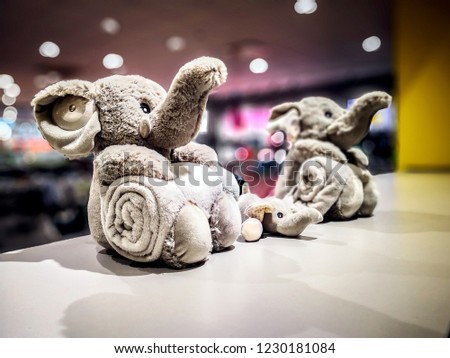 Figures of Family of three Grey adorable plusor or furry toys elephant with towel on blurry background of a shop as template for greeting card with copy space for text or message at the bottom.