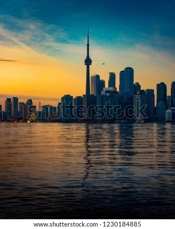 TORONTO CITY SKYLINE AT SUNSET - Beautiful scene of downtown cityscape with airplane flying in sky past tall office buildings and tower. Blue and orange colors reflecting in lake. Toronto, Canada