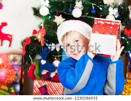 beautiful bright cheerful happy child boy is very happy gift presented for Christmas and New year emotionally surprised and cowardly gift near the ear listening to what's inside