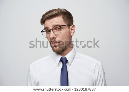 The young man looks through his glasses incredulously, evaluatively, thinks how much he can trust, is it lucrative practice, makes a decision assessing the risks, isolated over white background