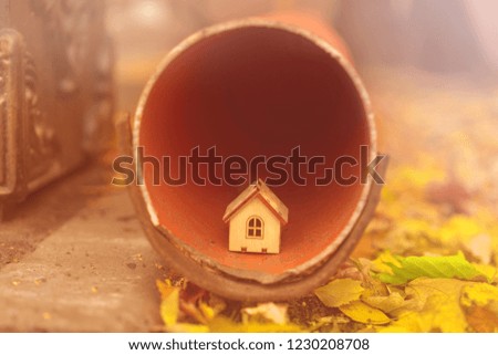 Miniature model of house on edge rainwater pipe with autumn leaves around