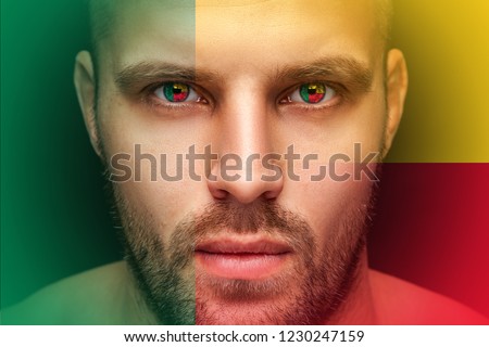 Portrait of a young serious man, in whose eyes the reflected national flag of Benin, against an isolated black background and flag