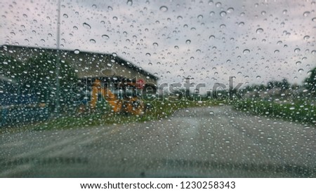 De focused image of rain falling on the road, looking out the window. Blurry car silhouette. Rain drops on window, rainy weather.