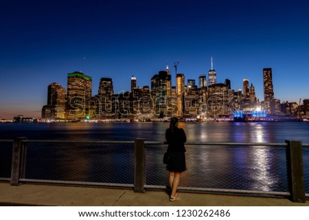 Lonely young woman standing on pier of the Granite prospect of Brooklyn Heights park wanting Manhattan skyline  after sunset