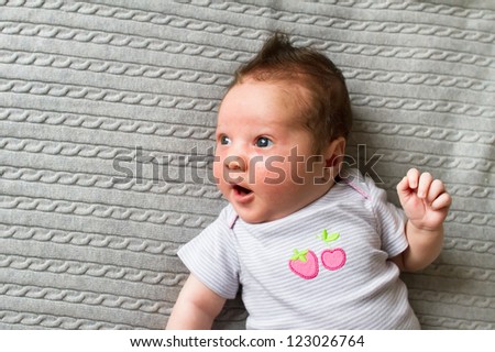 Sweet new born baby in a grey shirt with strawberry picture on a grey knitted blanket