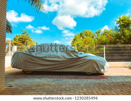 Car under a protective cover parked on the street Royalty-Free Stock Photo #1230285496