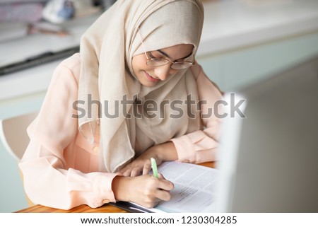 Young muslim  student writing and working in traditional clothes.