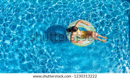 Aerial drone view of little girl in swimming pool from above, kid swims on inflatable ring donut , child has fun in blue water on family vacation resort
