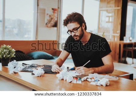Handsome Freelance Male Artist Painting on Paper. Closeup Portrait of Young Painter Sitting at Wooden Desk Focused and Concentrated on Art Project. Freelance Artist Concept