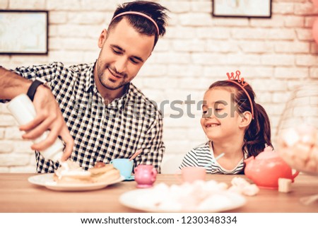 Father and Daughter on Sofa. Spend Time Together. Father's day. White Interior. Headband Hair on Head. Cakes on Plates. Bottle with Topping in Hand. Father Make Cupcake. Girl with Hairhoops.