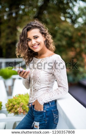 Young latin woman making self portrait on her smart phone digital camera while sitting in sidewalk cafe during lunch break. Pretty female posing while photographing herself for social network picture