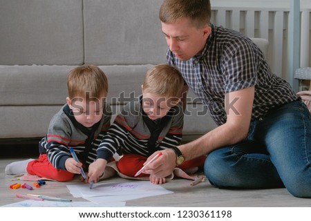 Family dad and two twin brothers draw together markers and felt pens sitting on the floor.
