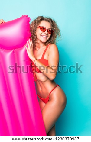 Young attractive woman in red bikini and sunglasses posing with pink inflatable mattress, isolated on green background