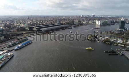 Aerial bird eye picture of IJ Amsterdam showing the main railway station and several landmarks docked tourist boats and ferry heading to northern part of the city