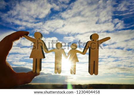 male hand hold wooden family  figure, sign against blue, yellow sky background with sun rays