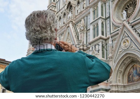Male tourist in a sweater with gray curly hair takes pictures on the phone Cathedral of Santa Maria del Fiore is the main attraction of Florence, Italy