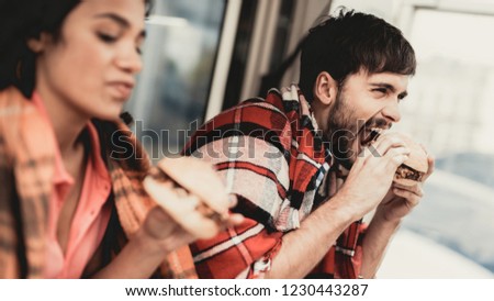 Young Couple in Checkered Plaids Eating Burgers. Street Food Concept. Food in Town. Selling Snacks. Girfriend and Boyfriend. Summer Day. Square in European City. Smiling People in Blanket.