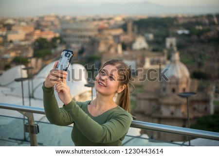 young woman wearing green pullover on the roof in front of Colosseum, Rome, Italy, makes selfie with her smartphone