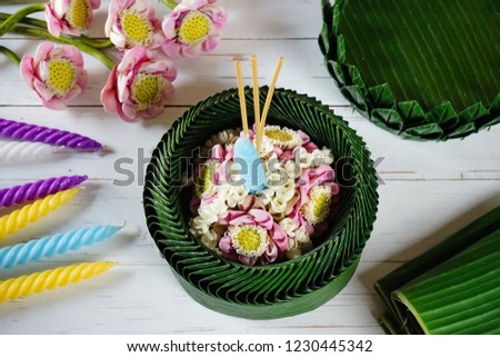 Loy Krathong Festival in Thailand concept lotus shaped banana leaves vessel or Krathong in Thai language contained a candle, three joss sticks and some flowers on vintage white painted wooden table.