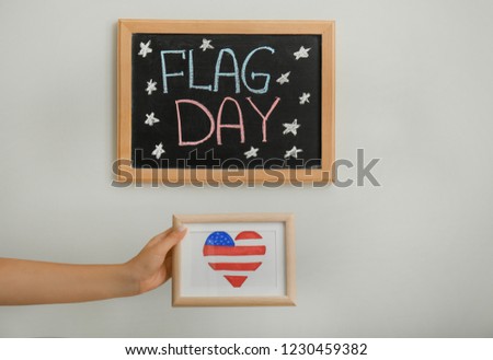 Woman holding picture with heart shaped drawing of American national flag on light background