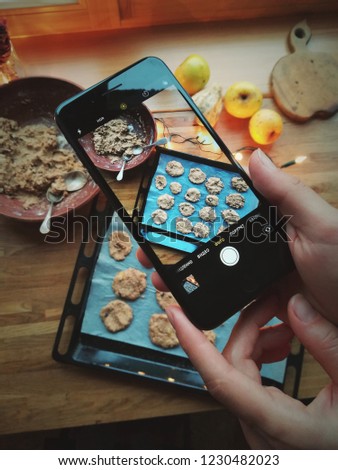 female hands close up holding mobile phone making photo of Christmas cakes cookies on baking form. Woman taking picture with smartphone top view of rustic wooden table process cooking sweet bakery 