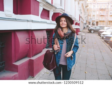 Attractive modern woman walking.Fashionable young woman walking in street in the city wearing jeans, sweater,black hat and backpack.Fashion spring photo,old city 
background.Copy space