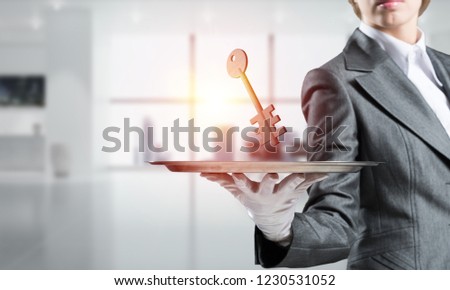 Closeup of waitress's hand in white glove presenting stone key symbol on metal tray with office view on background. 3D rendering.