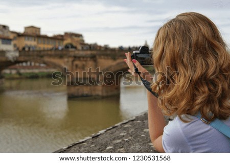 The girl the blonde with a blue backpack stands on the embankment of the river against the background of the gold bridge in Florence, Italy