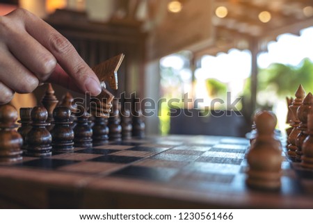 Closeup image of a hand holding and moving a horse in wooden chessboard game