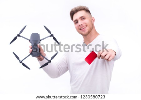 A young man is holding a flying drone and credit card in his hands on a white background. Theme selling and buying drones