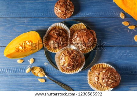 Delicious muffins with sunflower seeds and cut pumpkin on color wooden table