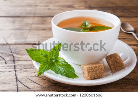 Cup of hot tea with mint and brown sugar on a wooden table.