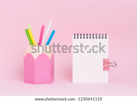 Mock up picture of empty notebook and pencil holder on pink background.