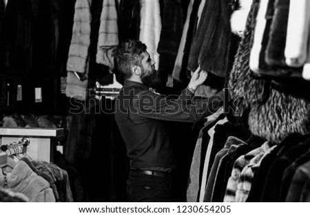 Guy looks at fur coat. Luxury shopping concept. Man with beard and mustache looking for fur coat. Macho with furry coats on background.