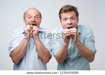 Two stunned men react on sudden news, keeps mouthes opened, stare at camera. Father and son got news about their wife pregnancy.