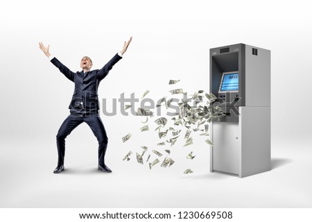 A happy businessman stands on a white background near an ATM machine with many dollar banknotes flying around. Receiving salary. Unbelievable income. Getting rich fast.