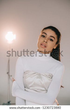 pretty african american girl in white turtle neck looking at camera in studio with spotlight