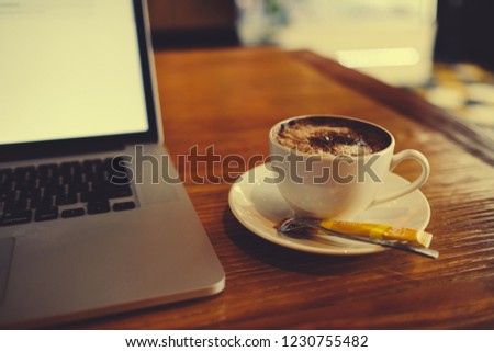 A cup of cappuccino coffee with laptop on table. Royalty high quality free stock image of capuccino coffee with laptop for working in a coffee shop. Beautiful workspace with retro and vintage style 