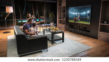 A family is watching a soccer moment on the TV and celebrating a goal, sitting on the couch in the living room. The living room is made in 3D. Royalty-Free Stock Photo #1230788584
