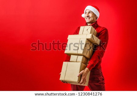 Portrait of one handsome new year man in red santa claus christmas hat with fur holding present box in studio on purple background, horizontal picture
