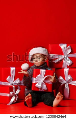 Smiling funny child boy in Santa red hat stretched his hand to the side.holding Christmas gift ,  on red background. Christmas concept.