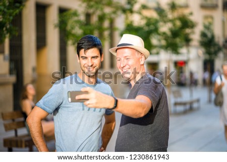 Two male friends taking selfie in the city using smartphone