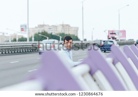The guy is sitting near the road on the bridge